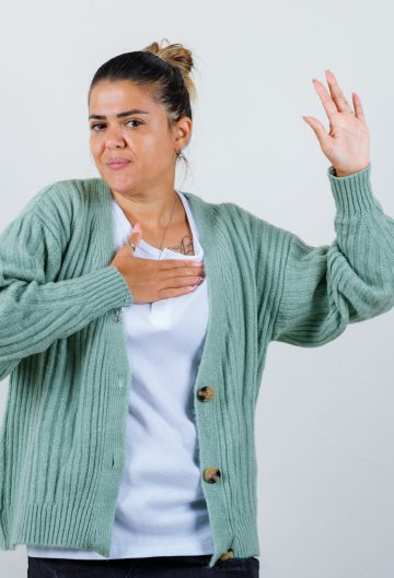 mujer-joven-en-camiseta-blanca-y-cardigan-verde-menta-sosteniendo-la-mano-en-el-pecho-mientras-levanta-la-mano-para-saludar-y-lucir-feliz-scaled.jpg